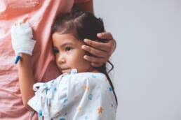 Sick hospitalized child hugging nurse in hospital